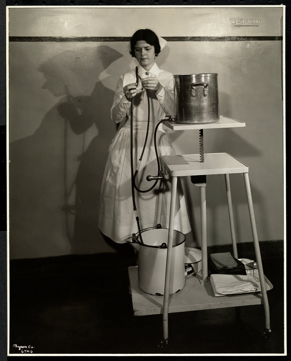 Egy ápolónő, aki egy speciális készüléket mutat be csövekkel, ellátó- és szemetesvödrökkel a Sloan Maternity Hospital-ban, Broadway és 168th Street, New York, 1932 (ezüst zselatin nyomat) alkotó: Byron Company